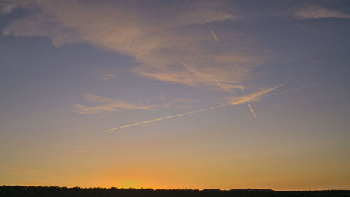 Low angle view of vapor trails in sky during sunset