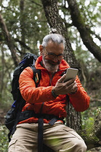 Man using phone while sitting on tree