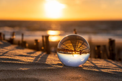 Close-up of crystal ball on sea against sky during sunset