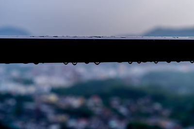 Close-up of raindrops on silhouette metal against sky