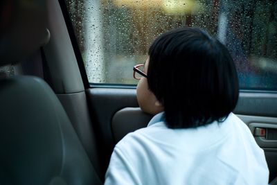 Rear view of woman seen through wet window