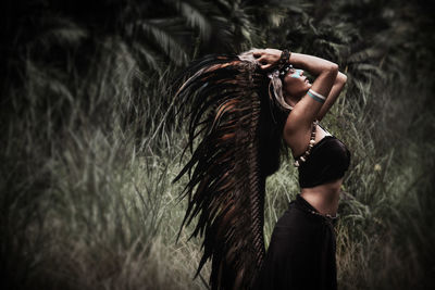 Side view of woman with arms raised standing outdoors