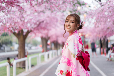 Portrait of young woman with pink cherry standing against trees