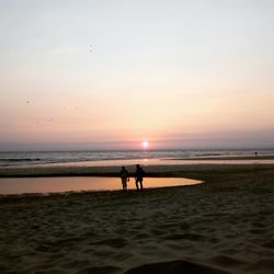 Silhouette people on beach against sky during sunset