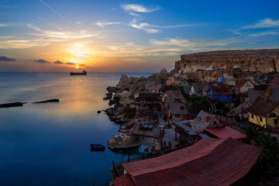 Houses at sea shore against sky during sunset