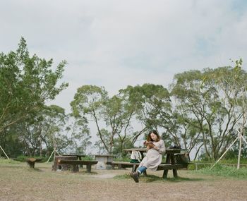 Woman sitting on bench against sky