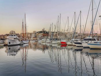 Sailboats moored in harbor at sunset