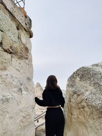 Rear view of woman standing on rock against sky