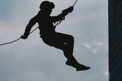 Low angle view of silhouette man jumping against sky