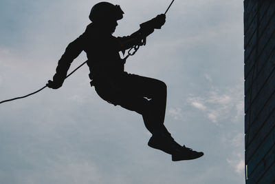 Low angle view of silhouette person hanging against sky