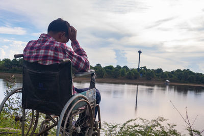 Man sitting by lake against sky