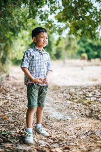 Cute boy looking away and standing against trees