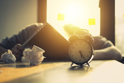 Stressed businessman with crumpled paper balls and alarm clock at desk