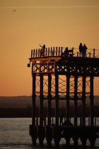 Silhouette people standing on pier by sea against orange sky