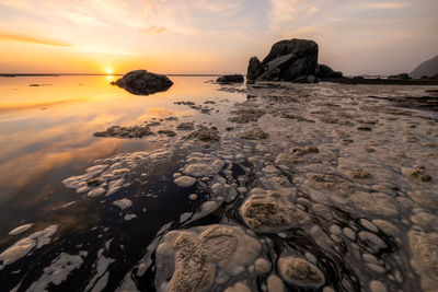 Rocks on beach against sky during sunset