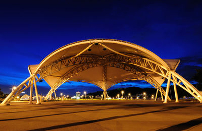 Illuminated bridge against blue sky at night