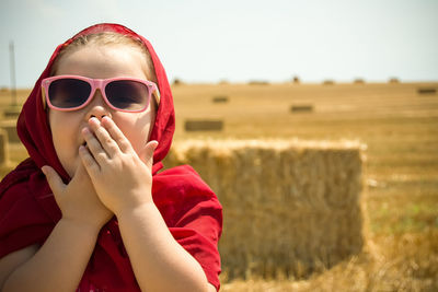 Portrait of girl wearing sunglasses and scarf covering mouth while standing against field