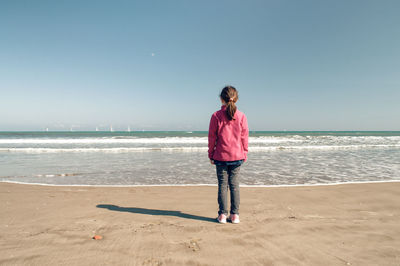Rear view of girl standing at beach against clear sky