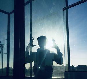 Silhouette man standing by glass window against bright sun