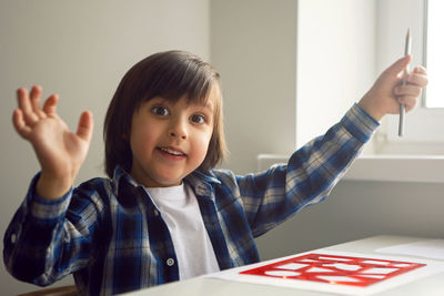 Boy child draws on paper with a ruler on a table sitting by the window