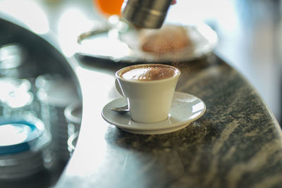 Pouring cocoa on cappuccino in a bar counter top