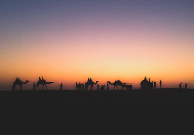 Silhouette people and camels at desert during sunset