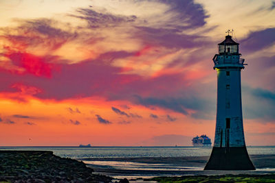 Lighthouse by sea against sky during sunset