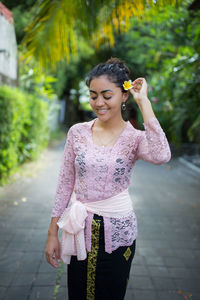 Beautiful young woman wearing flower on ear while standing on footpath
