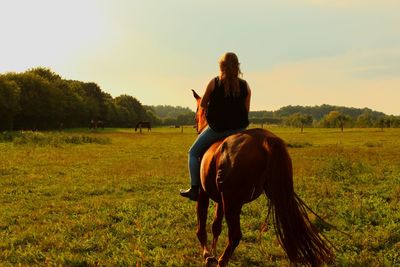 Young woman riding a horse on a field against sky