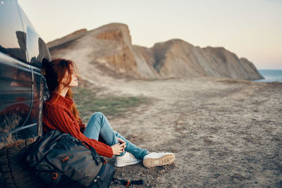 Woman sitting on rock by sea against sky