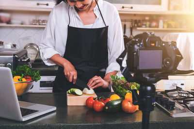 Woman slicing vegetables with camera in kitchen