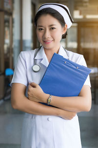 Portrait of female doctor holding file while standing in hospital