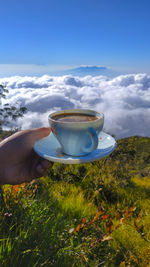 Man holding coffee cup against sky