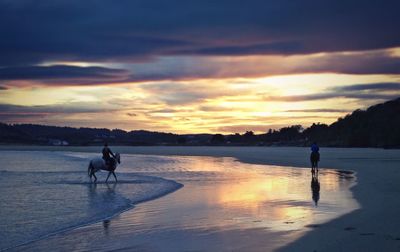 Silhouette people on beach against sky during sunset