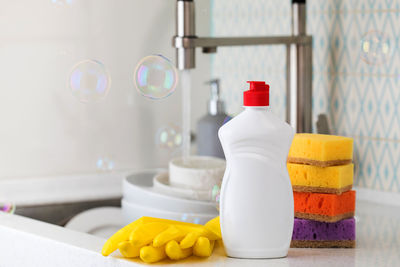 A white bottle with dishwashing gel, sponges and rubber gloves on the background of a sink 