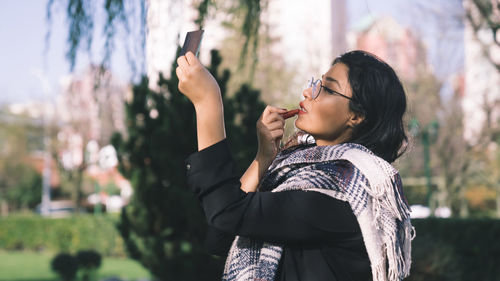 Young woman photographing with mobile phone standing outdoors