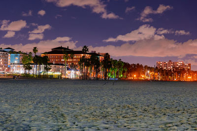 Illuminated buildings by sea against sky at night