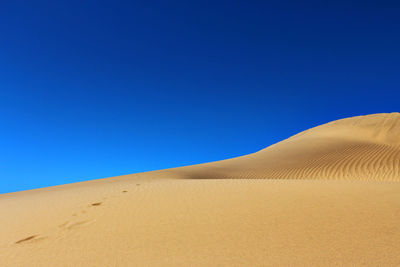 Sand dunes in desert against clear blue sky