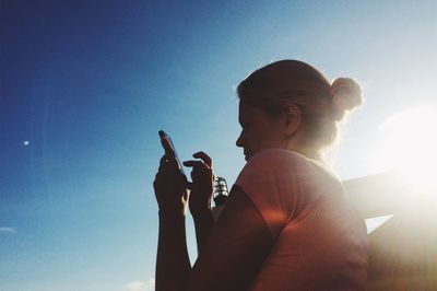 Woman using mobile phone against blue sky