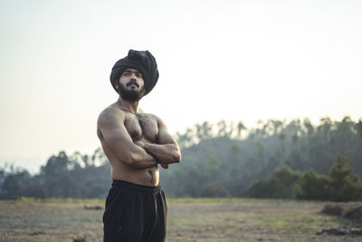 Full length of shirtless man standing on field against sky