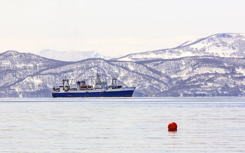 Large fishing vessel on the background of snow-covered hills and volcanoes 