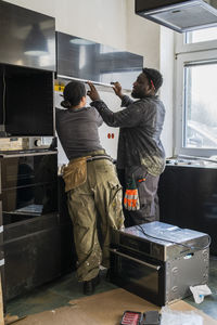 Multiracial male and female carpenters measuring cabinet in kitchen at home