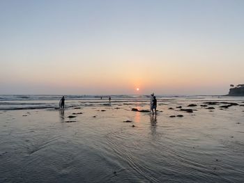 Silhouette people on beach against sky during sunset