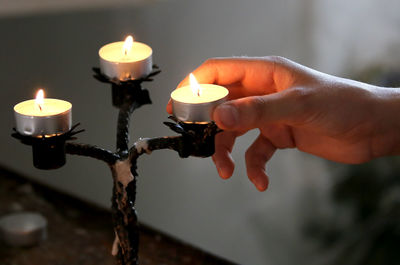 Close-up of hand holding lit tea light candle at table