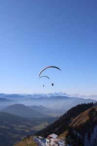 People paragliding against clear blue sky