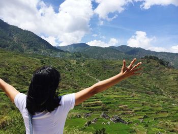 Rear view of woman with arms raised standing by landscape and mountains