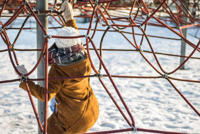 Rear view of woman climbing on ropes at snow covered park