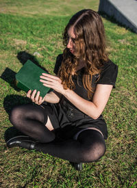 High angle view of woman holding book while sitting on field