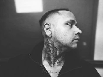 Man with tattooed neck looking away at home
