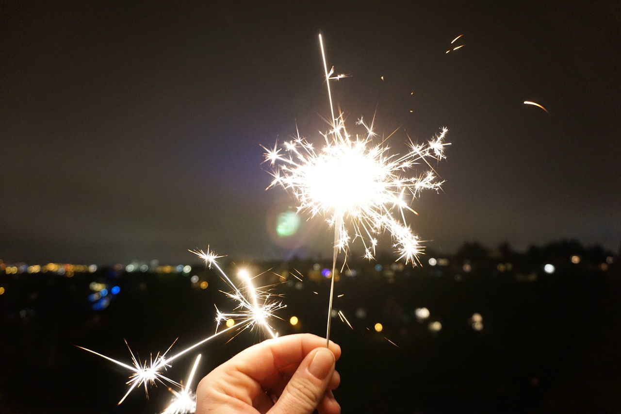 CLOSE-UP OF HAND HOLDING FIREWORK DISPLAY